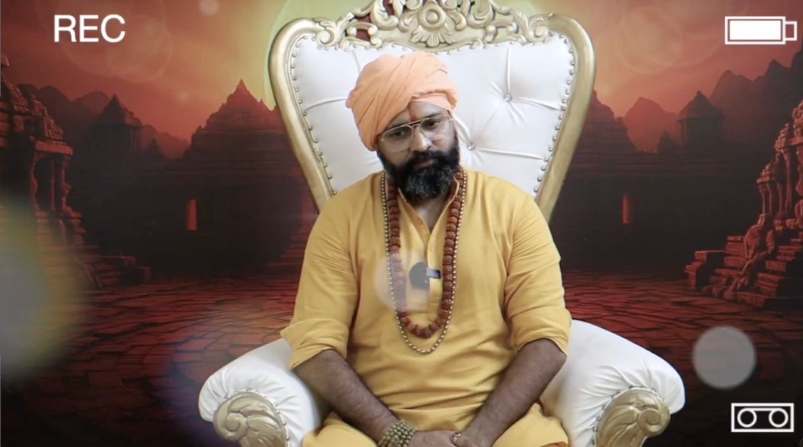 Kabeer Ji Maharaj सोने की कुर्सी पर बैठे recording कर रहे हैं — भगवा वस्त्र, रुद्राक्ष, पृष्ठभूमि में प्राचीन मंदिर। Daily Discourse session।