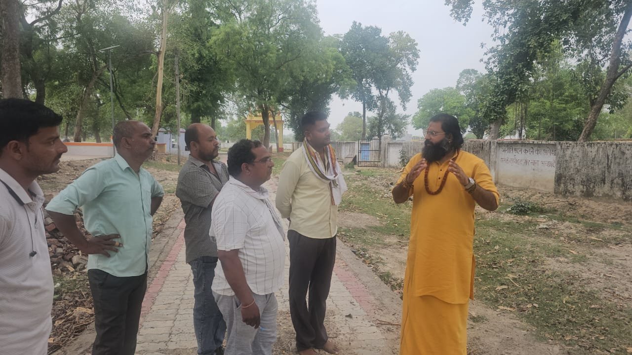 Kabeer Ji Maharaj एक पार्क में 5-6 व्यक्तियों के साथ खड़े होकर discussion कर रहे हैं। पृष्ठभूमि में पेड़ और मंदिर।