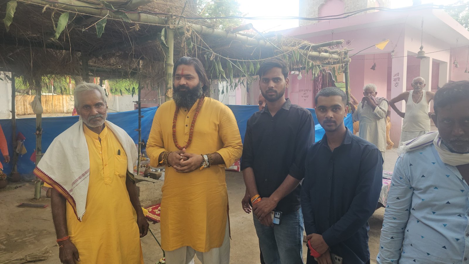 Kabeer Ji Maharaj (Kabeer Goswami) temple event में community के साथ — भगवा कुर्ता, rudraksh, जय माता दी wall। Janpad community building।