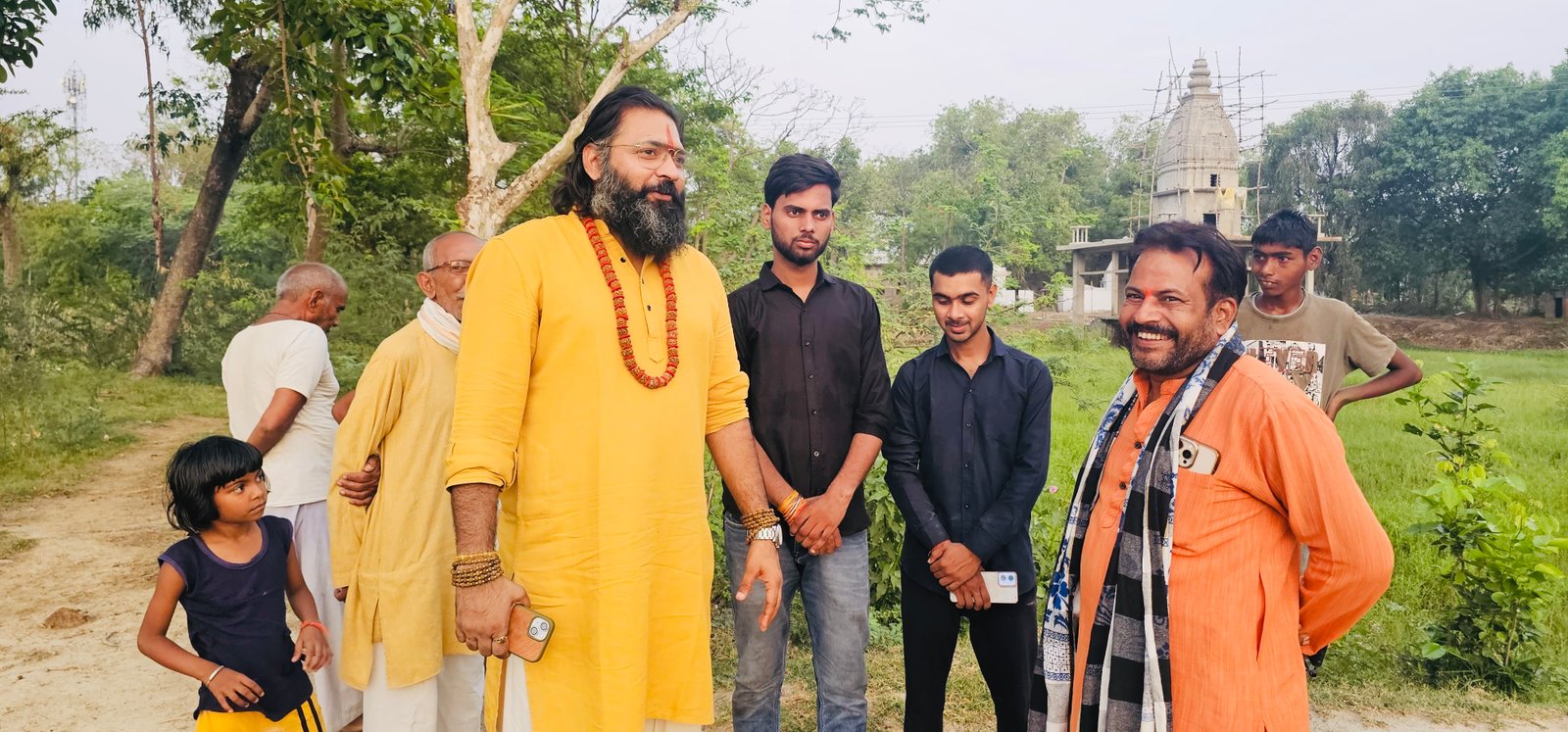 Kabeer Ji Maharaj village walk में community के साथ — पृष्ठभूमि में temple shikhara, हरे खेत, बच्चे, स्थानीय लोग। Janpad revolution।